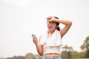 A tired woman holds a small fan and wipes her sweat on her face while walking outdoors on a hot day. photo