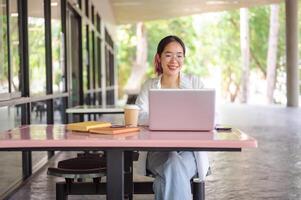 A young Asian female student working on her laptop while sitting at a table in her college canteen. photo