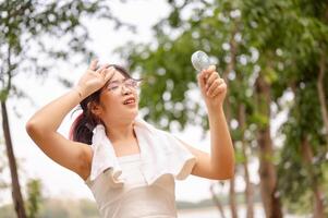 un mujer sostiene un pequeño ventilador y toallitas su sudor en su cara mientras caminando al aire libre en un caliente día. foto