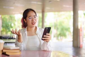 A perplexed young Asian female college student looks at her phone with a confused expression. photo