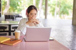 A focused female student working on her laptop while sitting at a table in her college cafeteria. photo