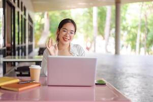 A female college student is having a meeting call while sitting at a table in a cafeteria. photo