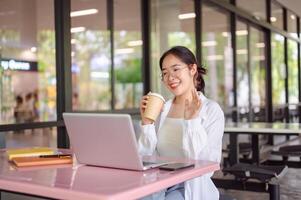 A female college student is having a meeting call while sitting at a table in a cafeteria. photo