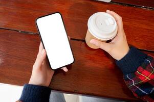 Close-up top view shot of a woman holding a coffee cup and using her smartphone at a table. photo