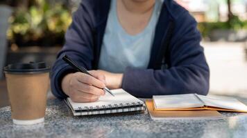 Woman taking notes in a spiral notepad while sitting at an outdoor table, working remotely at a cafe photo