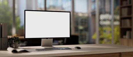 A computer mockup with a white screen and office supplies are arranged on a table in a modern office photo