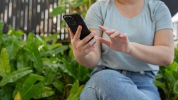 un recortado Disparo de un asiático mujer utilizando su teléfono inteligente mientras sentado en su hogar jardín. foto