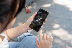 A close-up shot of a woman using the TikTok application on her iPhone while sitting outdoor. photo