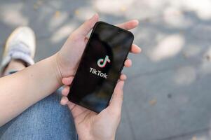 A close-up shot of a woman using the TikTok application on her iPhone while sitting outdoor. photo