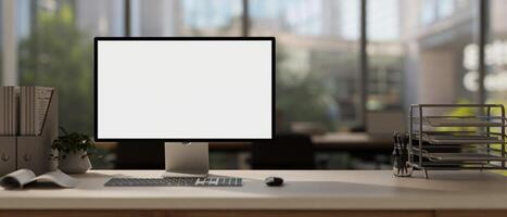 A computer mockup with a white screen and office supplies are arranged on a table in a modern office photo