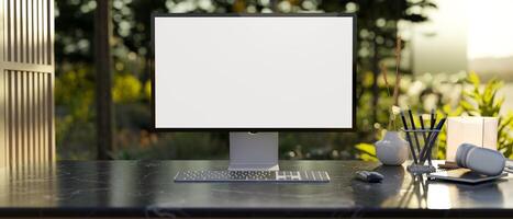 A modern workspace features a computer mockup on a table with a green garden in the background. photo