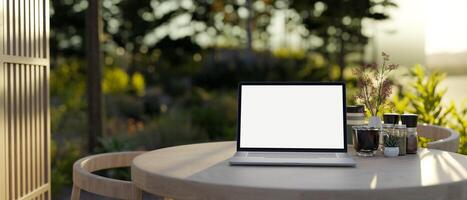 A laptop computer mockup on a wooden table on an outdoor patio lounge with a green garden. photo