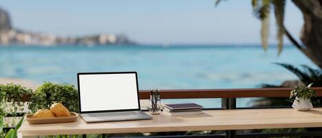 A remote workplace with a laptop mockup on a table on a balcony with a beautiful ocean sea view. photo