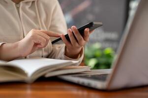 A woman in a white hoodie using her smartphone while working remotely at a cafe. photo