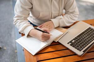 A woman writing in her notebook, listing ideas in a book while working remotely at an outdoor cafe. photo