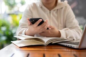 A woman in a white hoodie using her smartphone while working remotely at a cafe. photo