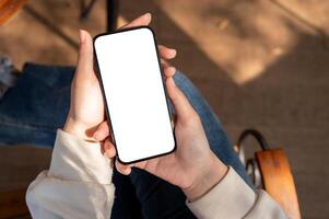 un blanco pantalla teléfono inteligente Bosquejo en un mujer mano como ella se sienta en un banco al aire libre, utilizando su teléfono. foto