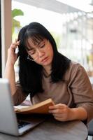 un grave y pensativo joven asiático hembra Universidad estudiante es leyendo un libro en un cafetería. foto