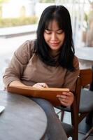 A positive Asian female is keeping her diary or listing her ideas in a book while sitting in a cafe. photo