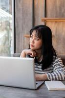 Woman is looking out the window and contemplating something while working remotely at a coffee shop. photo