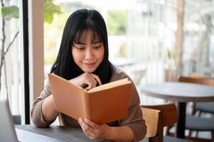 A happy Asian female college student is diligently reading a book in a cafe co-working space. photo