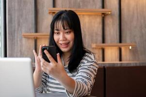 A cheerful young Asian woman is talking on a call with her friend while relaxing in a cafe. photo