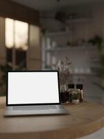 Close-up image of a white-screen laptop computer mockup on a wooden table in a room. photo