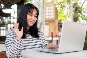 A positive Asian woman is having an online meeting with her team, working remotely at a cafe. photo