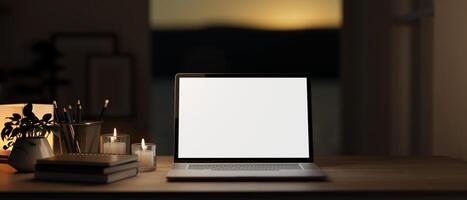 A table with a white-screen laptop mockup, burning candles, and decor in a dark room at night. photo