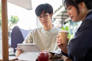 Two young Asian friends or colleagues are discussing and working on a project together at a cafe. photo