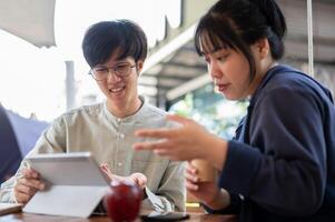 Two young Asian friends or colleagues are discussing and working on a project together at a cafe. photo