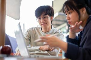 Two happy young Asian college students are discussing and working on a project in a cafe together. photo