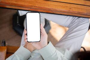 A man using his smartphone at a table in a cafe, with a white-screen smartphone mockup. photo