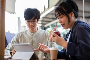 Two young Asian friends or colleagues are discussing and working on a project together at a cafe. photo