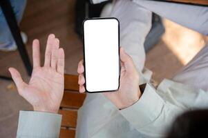 An unhappy, dissatisfied man showing his palm while using his smartphone at a table indoors. photo