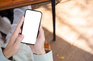 A man using his smartphone at a table in a cafe, with a white-screen smartphone mockup. photo