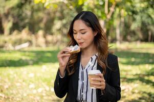 A businesswoman is having a quick breakfast in a city park, eating a sandwich and drinking coffee. photo