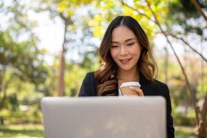 A beautiful Asian businesswoman is working remotely in a park in the afternoon. photo