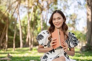 A beautiful Asian woman in a cute dress is reading a book in a green park on a bright, sunny day. photo