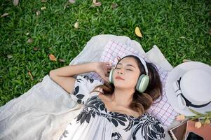 A beautiful woman falls asleep while listening to music on her headphones on a picnic mat in a park. photo