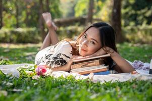 A woman is lying on a picnic mat, putting her head on a stack of books, and enjoying a picnic. photo