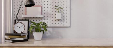 A tabletop with books, a clock, a table lamp, a potted plant, and a space against the wall. photo