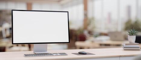 un pantalla blanca ordenador personal computadora en un minimalista madera mesa en un contemporáneo oficina trabajo colaborativo espacio. foto