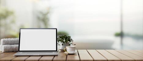 A white-screen laptop computer on a wooden table with a blurred background of a luxurious bathroom. photo