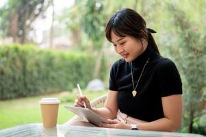 An attractive Asian woman sits at an outdoor table in a garden or backyard using her digital tablet. photo