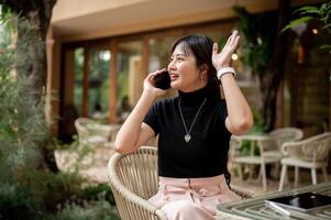 A woman sits at an outdoor table talking on the phone while waving her hand to call someone. photo