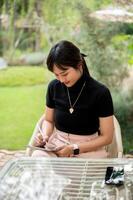 un atractivo asiático mujer se sienta a un al aire libre mesa en un jardín o patio interior utilizando su digital tableta. foto