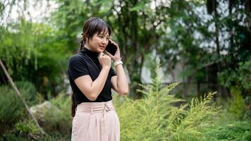 A positive, beautiful Asian woman talking on the phone while walking in a beautiful green garden. photo