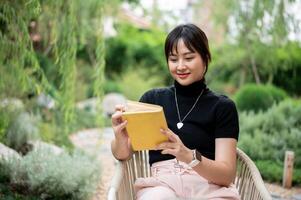 A positive Asian woman relaxing in a backyard and reading a book or writing her diary at a table. photo