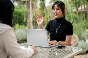 A cheerful Asian woman talking with her friend while working remotely in the garden. photo